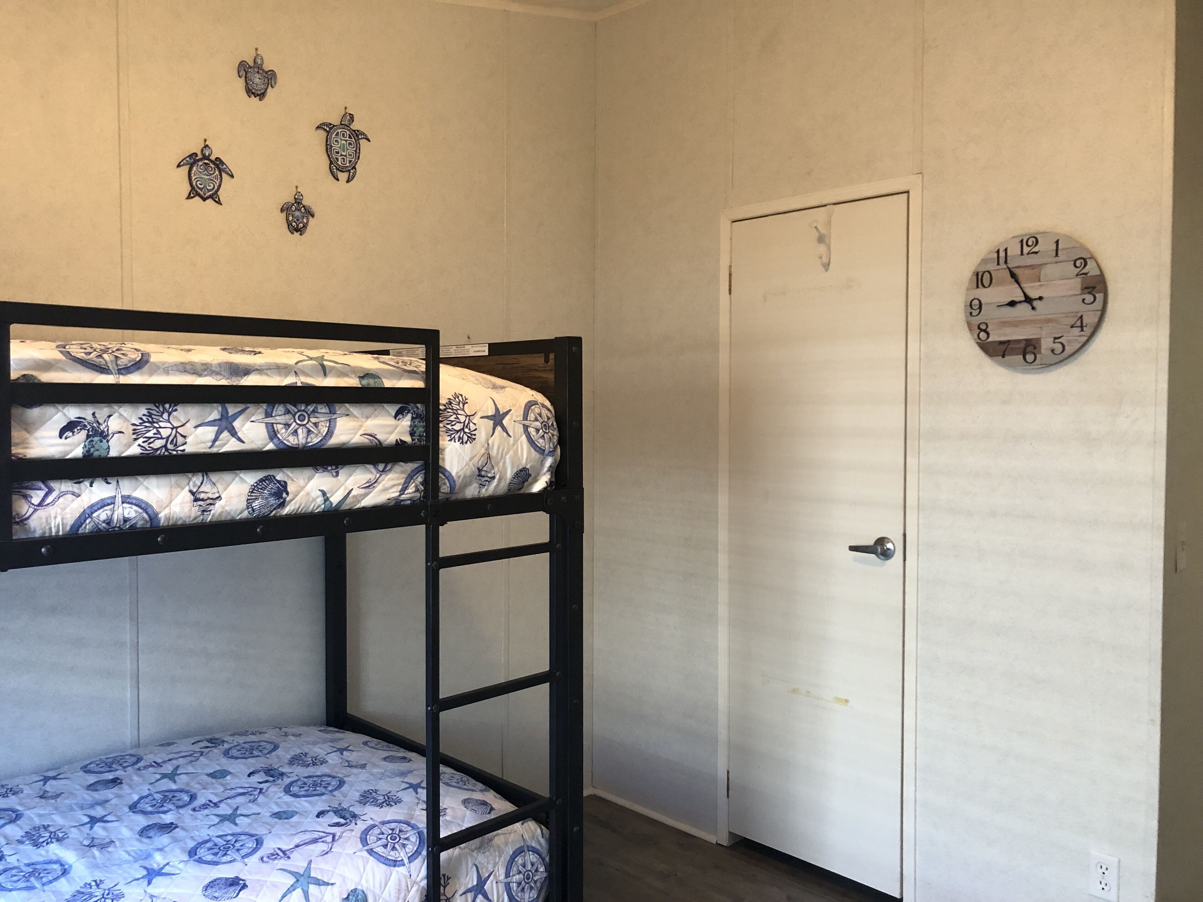A bunk bed with a nautical-themed bedding, a wall clock, and a door with a handle.