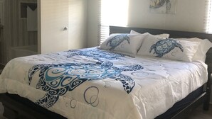 Un dormitorio con cama, ventilador de techo, ventana con persianas y un cuadro de tortuga en la pared.