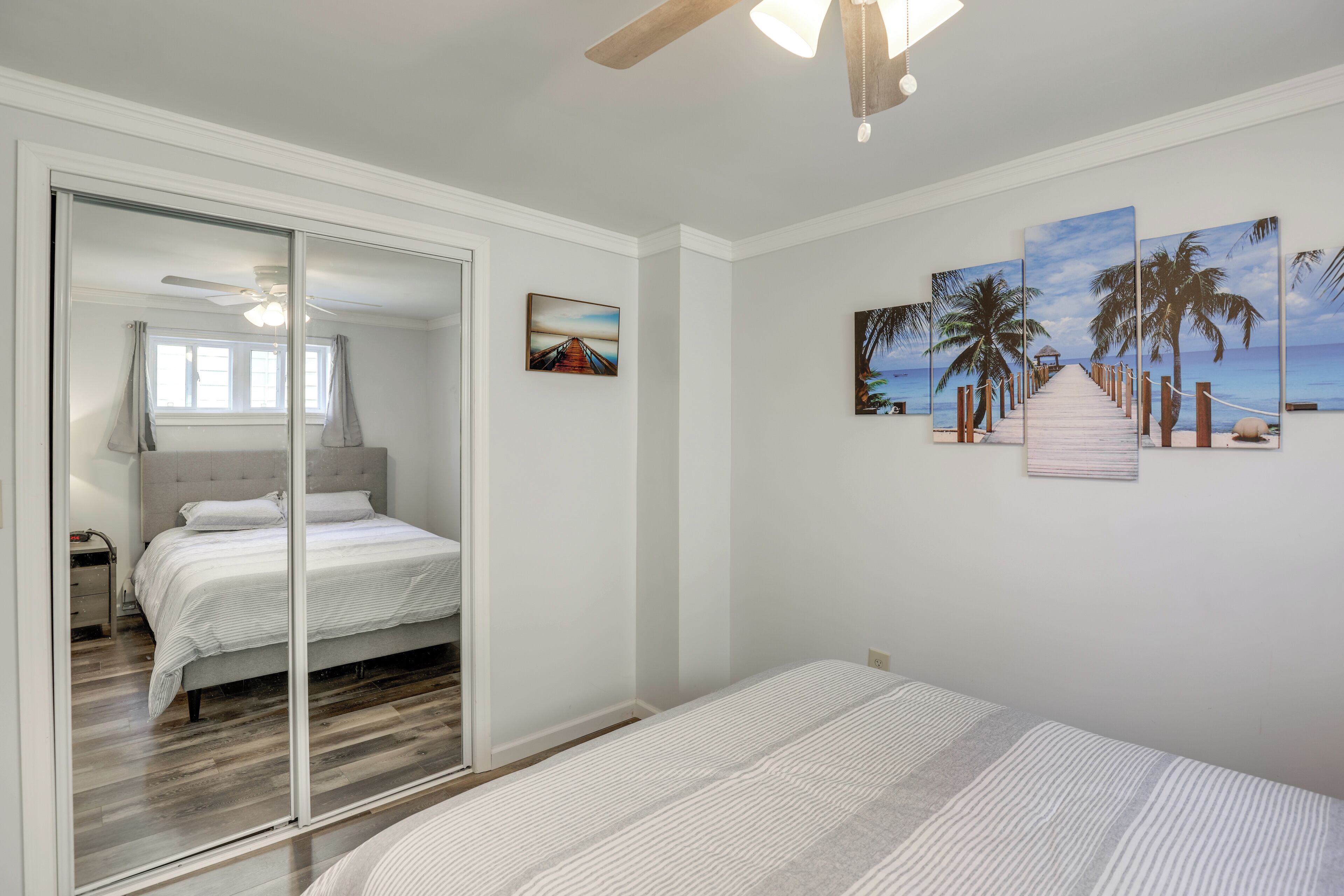 A bedroom with a bed, a sliding glass door leading to a bathroom, and a wall with three palm tree paintings.