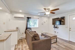 Ein modernes Wohnzimmer mit Deckenventilator, einem flachbildfernseher an der Wand, einem braunen Ledersofa, einem Holztisch und einem Fenster mit durchsichtigen Vorhängen.