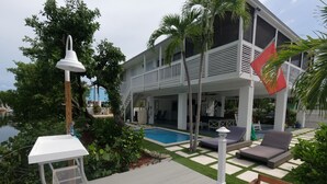 A poolside area with a lounge chair, a small table, and a pool. - Mermaid House: Heated Pool, Dual Dockage & Outdoor Bar on the Canal (Ramrod Key)