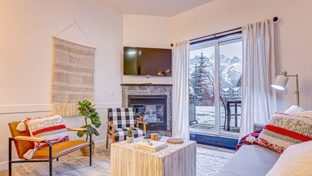 Una sala de estar acogedora con chimenea, un sofá, una mesa de centro y vistas a un paisaje nevado a través de grandes ventanales.