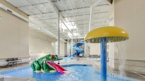 Un parque acuático interior con un tobogán, una fuente de agua y una estructura acuática con forma de rana.