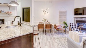 Una cocina moderna con encimeras de granito, un comedor con sillas de madera, una lámpara colgante y una chimenea.