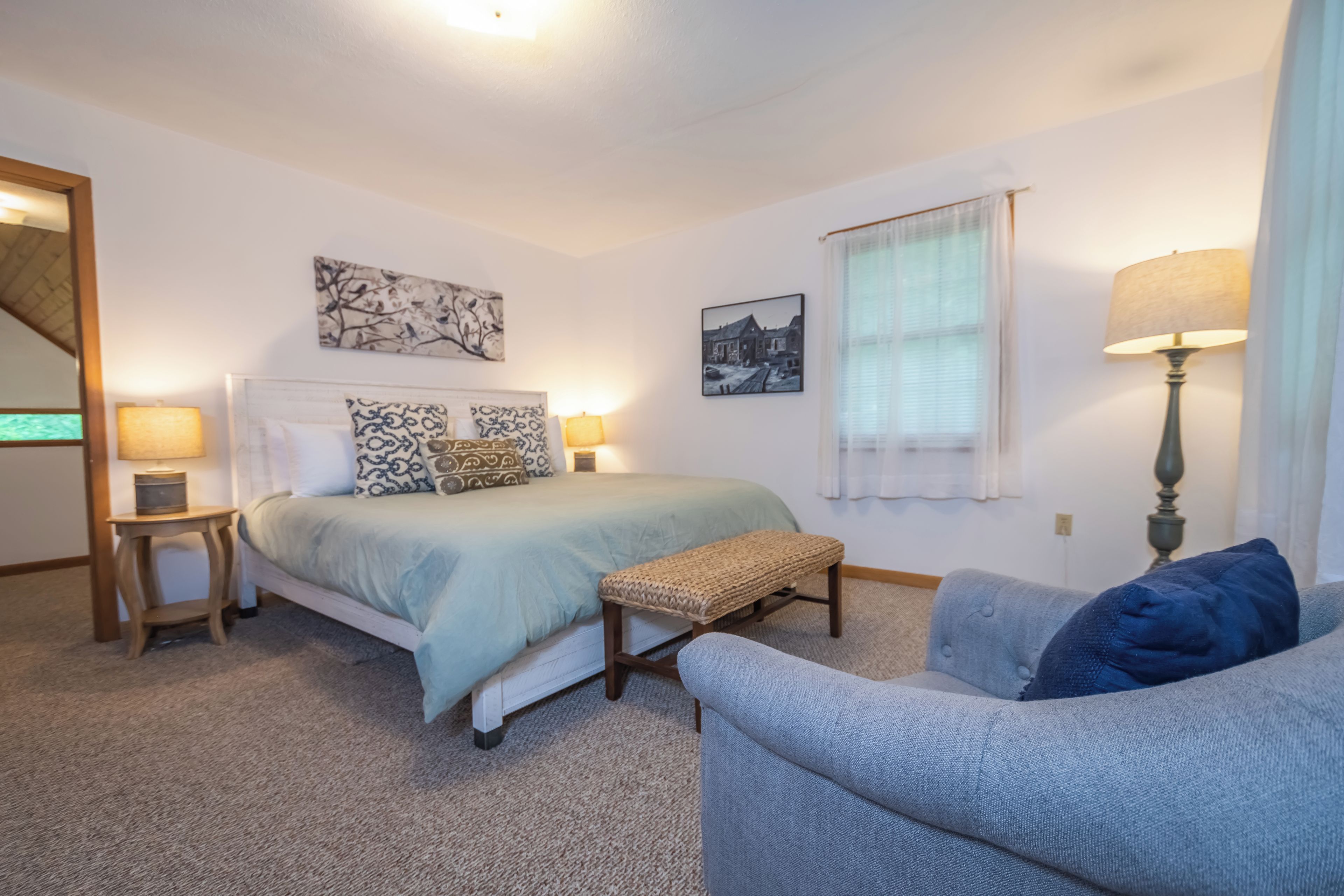 A bedroom with a bed, bedside tables, a bench, a chair, and a lamp.