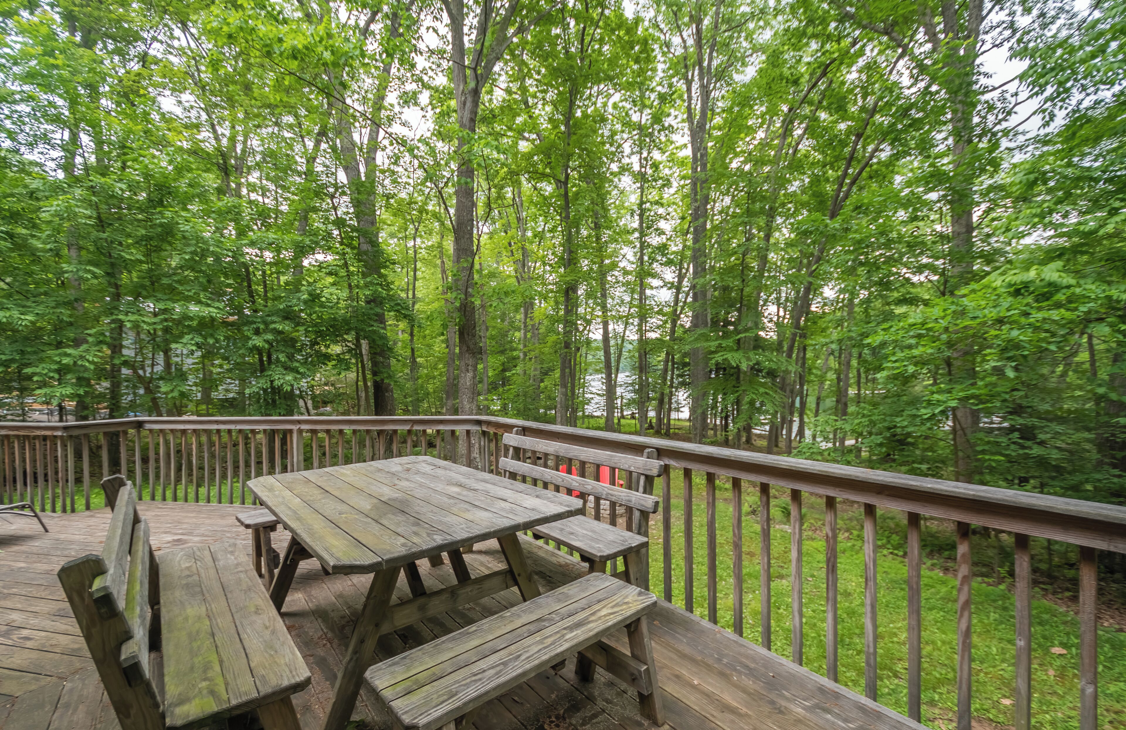 A wooden deck with picnic tables and benches, surrounded by tall trees.