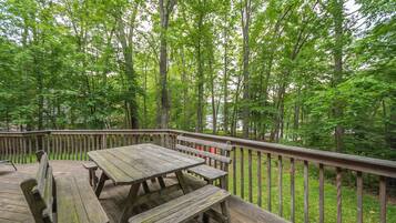 A wooden deck with picnic tables and benches, surrounded by tall trees.