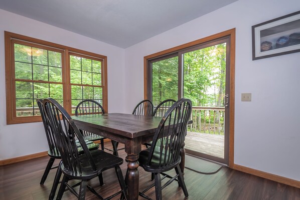 Un comedor con mesa y sillas de madera, ventanas amplias y una puerta que da a una terraza.