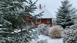 Ein rotes Haus, umgeben von schneebedeckten Bäumen und Sträuchern.