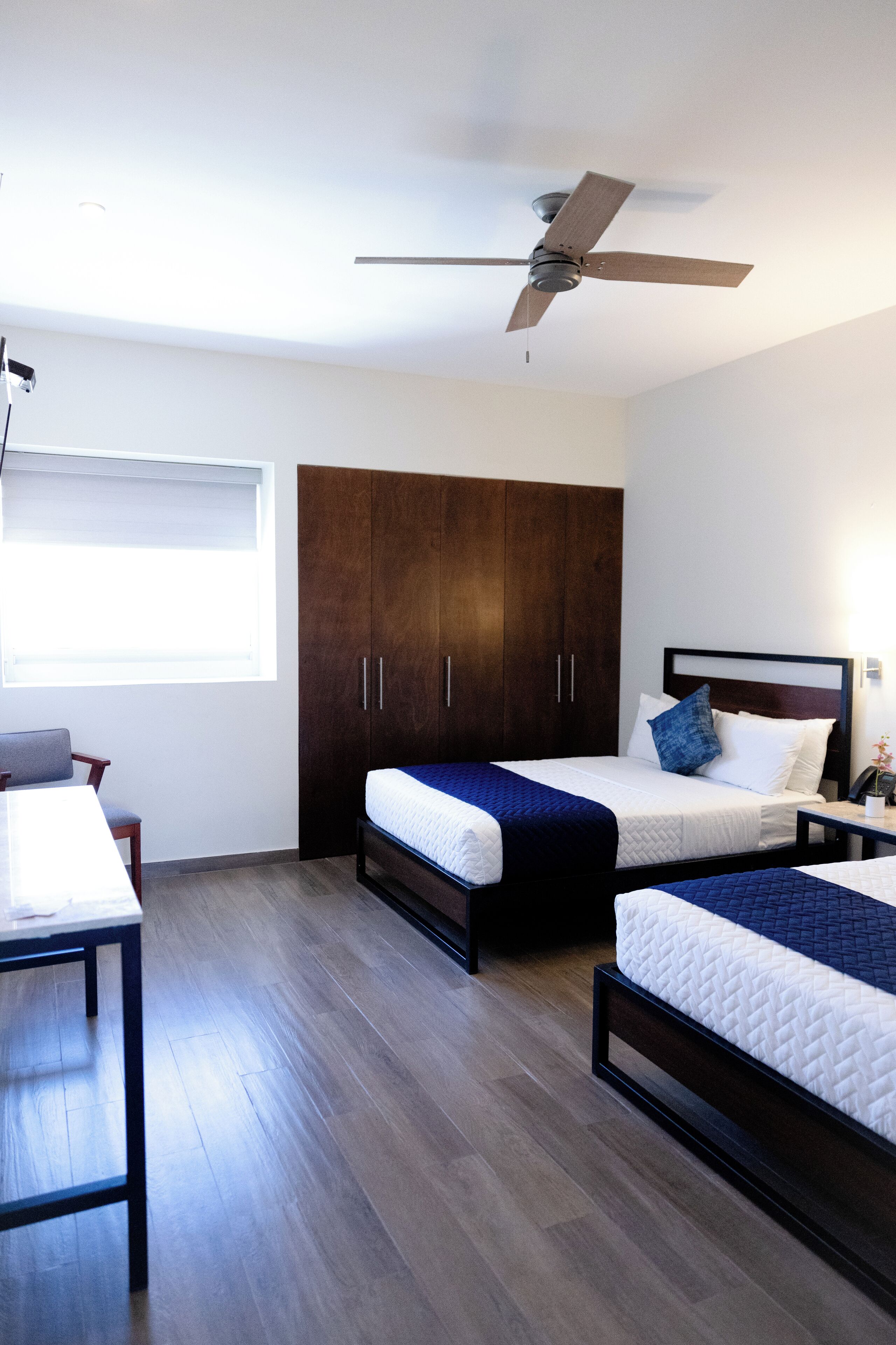 A bedroom with two beds, a wardrobe, a desk, and a ceiling fan.