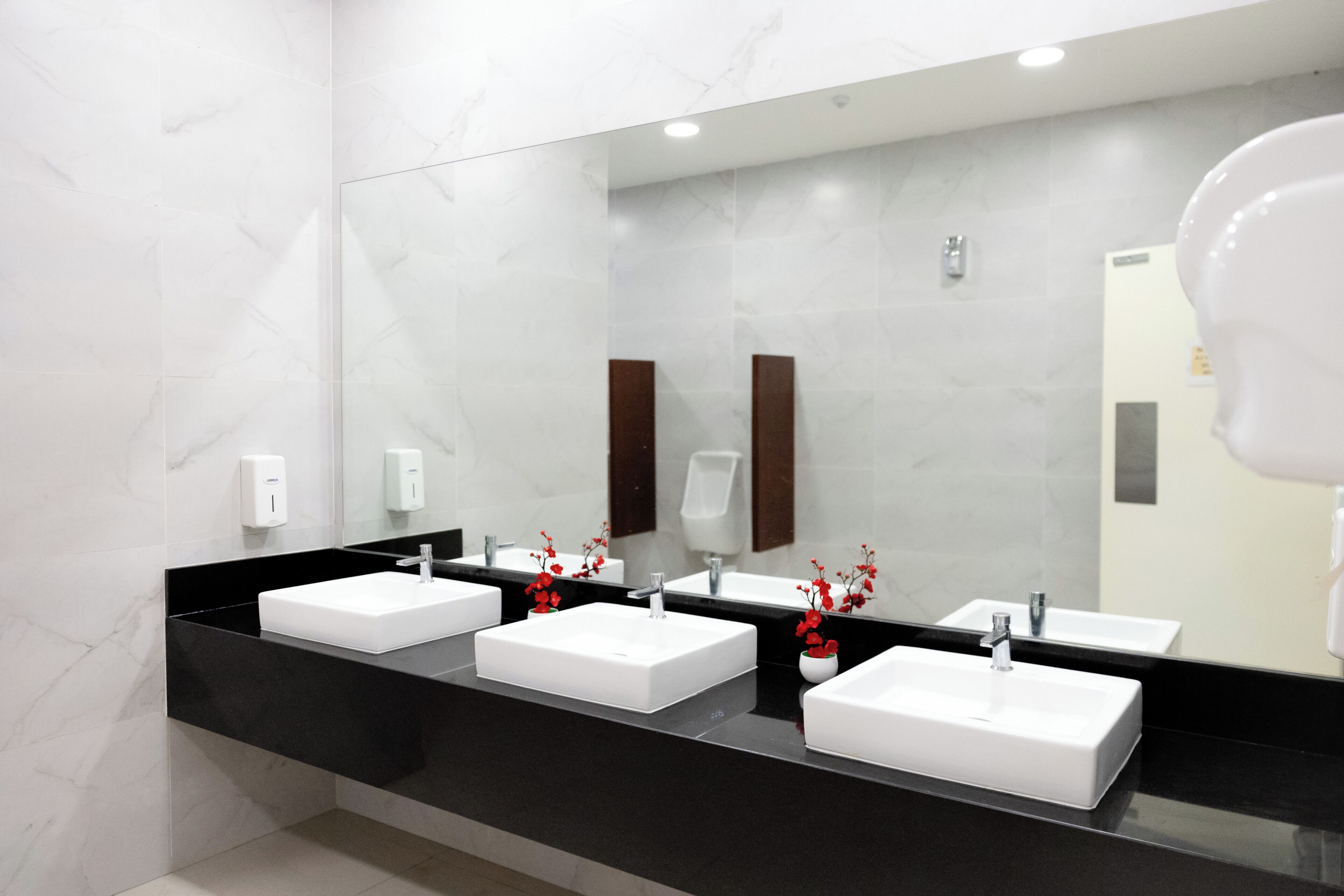 A modern bathroom with three white sinks, black countertops, and marble walls.