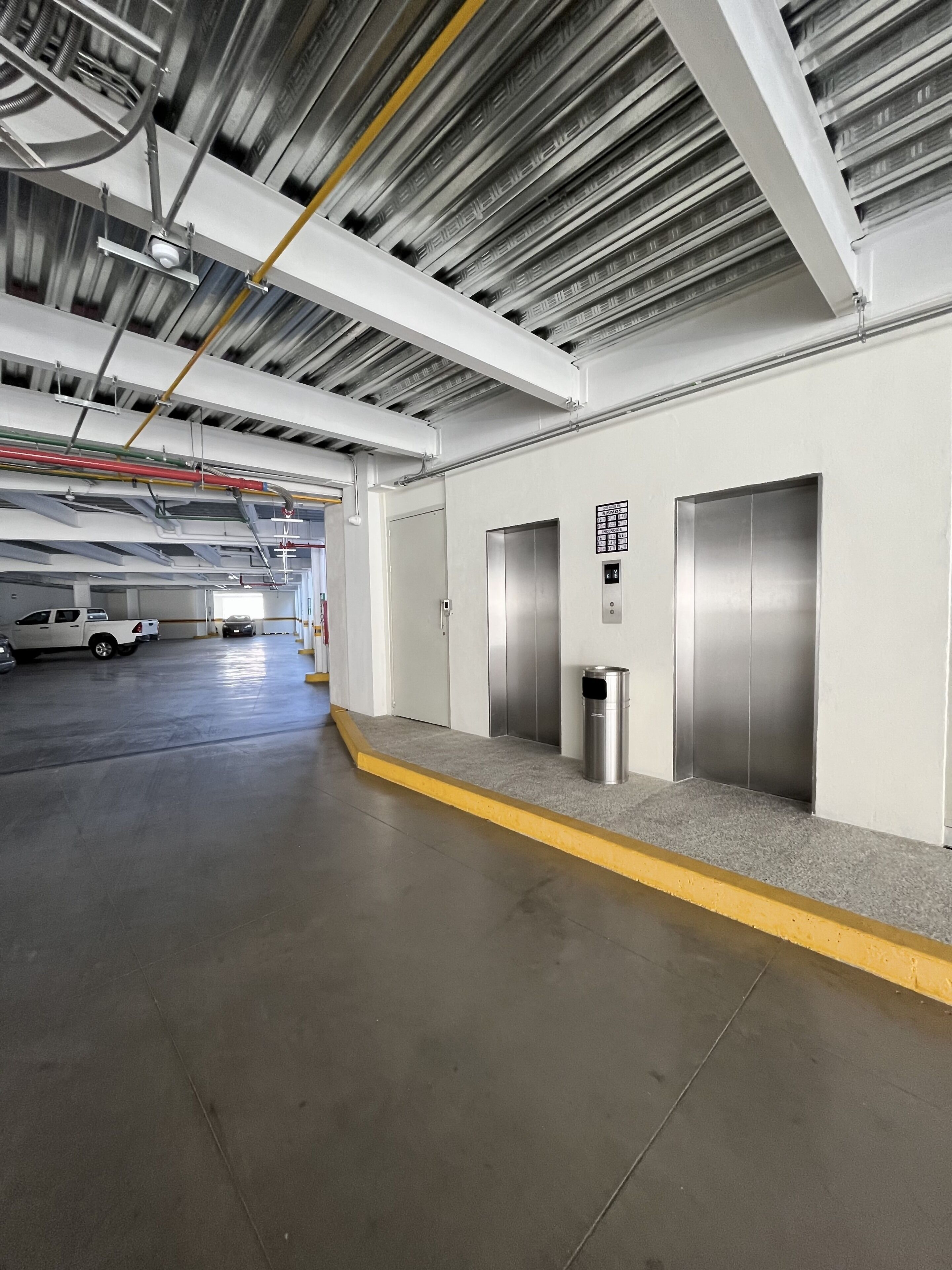 A clean, modern indoor parking garage with a concrete floor, metal walls, and two elevators.