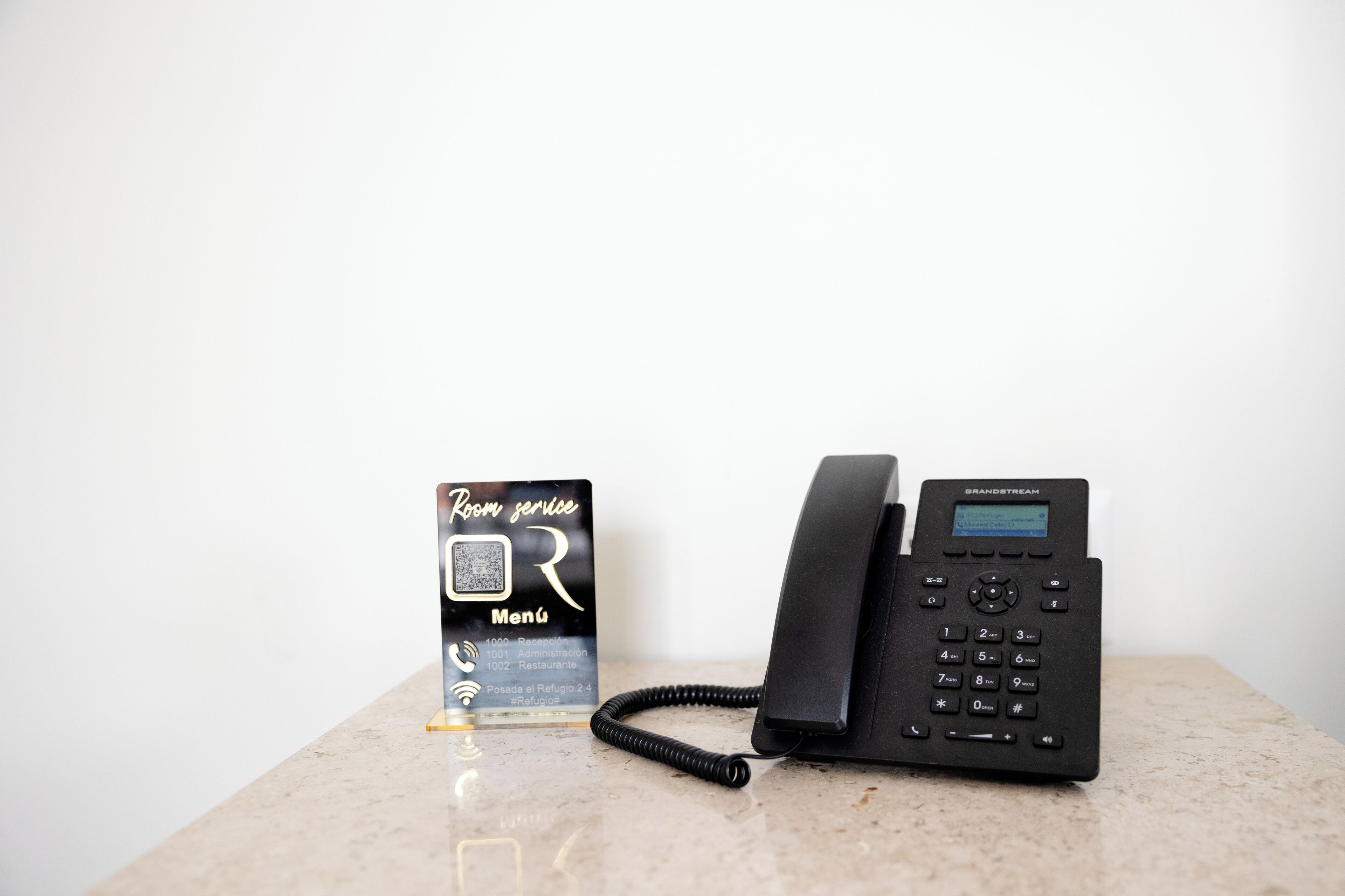 A Grandstream phone and a room service menu card on a marble surface.