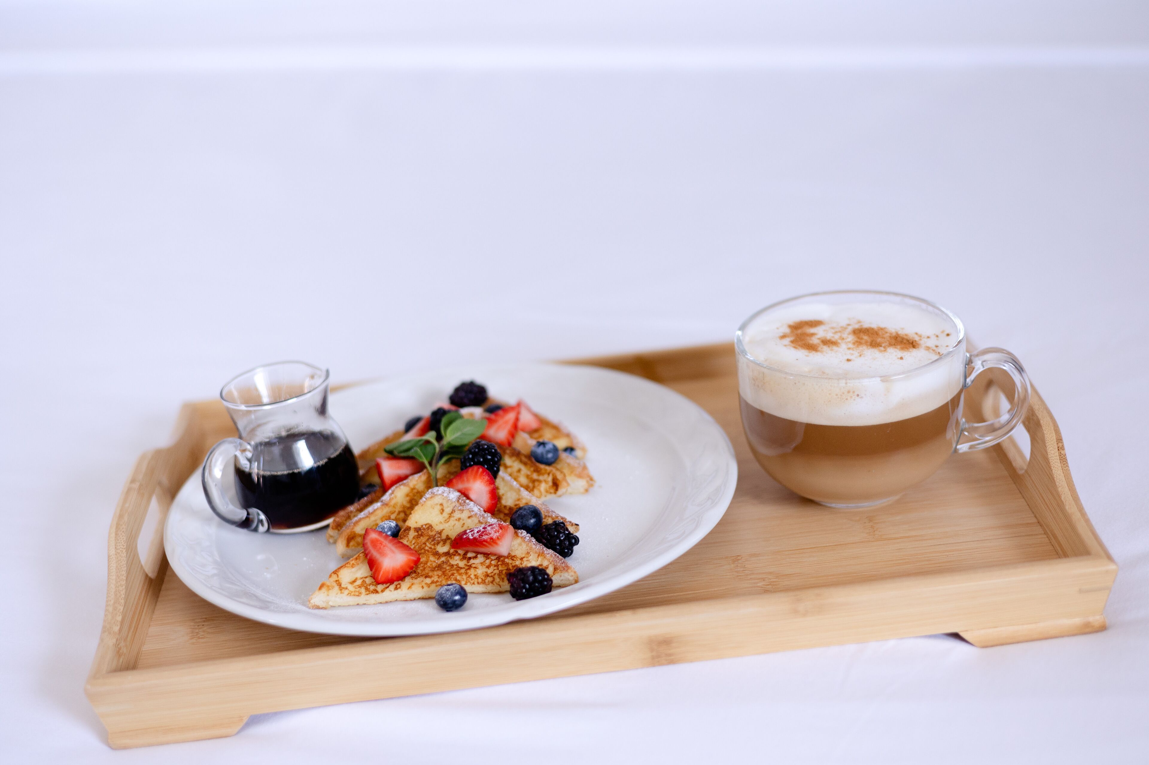 A breakfast tray with pancakes topped with strawberries, blueberries, and blackberries, a cup of coffee, and a small pitcher of syrup.