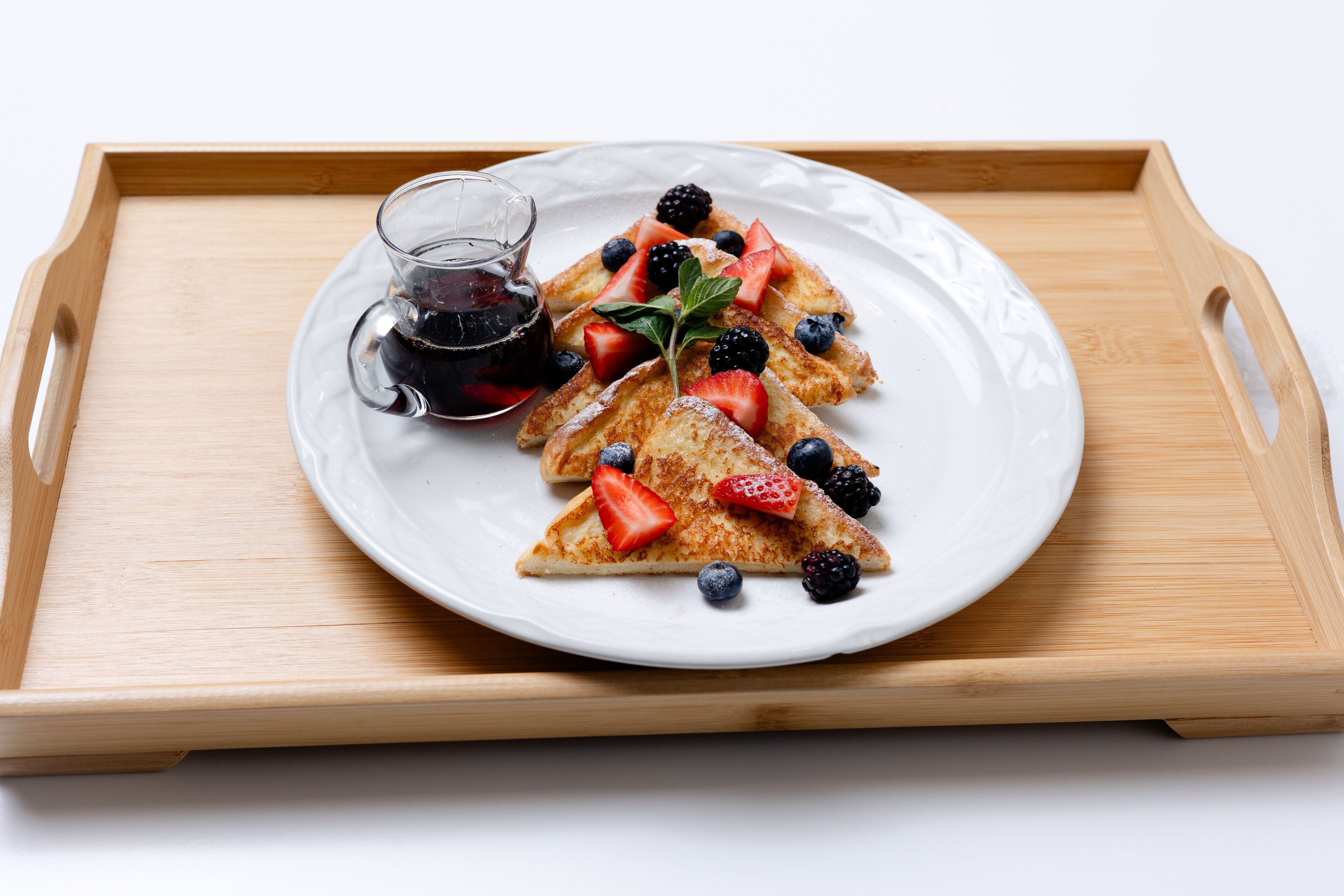 Une assiette de crêpes triangulaires garnies de fraises et de myrtilles, accompagnée d’un verre de sirop.