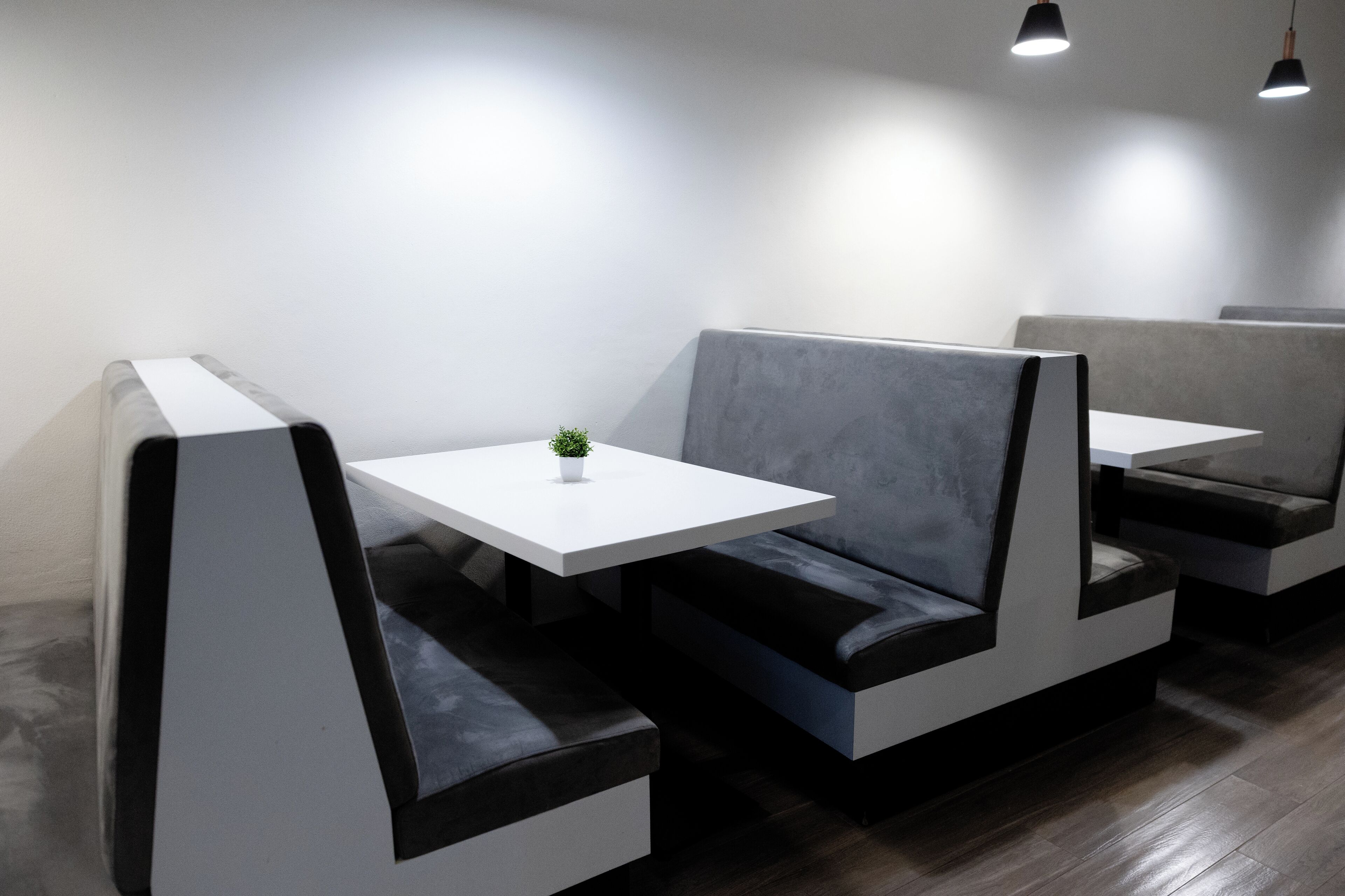 Un restaurant moderne avec un intérieur élégant, des banquettes et de petites tables, caractérisé par un design minimaliste et un revêtement de sol en bois foncé.