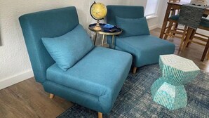 Two teal armchairs with a small round table between them, a globe, and a patterned ottoman.