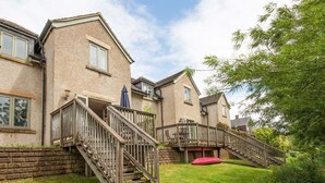 Une maison à deux étages avec un escalier en bois menant à un balcon, un mur en briques et une cour gazonnée.