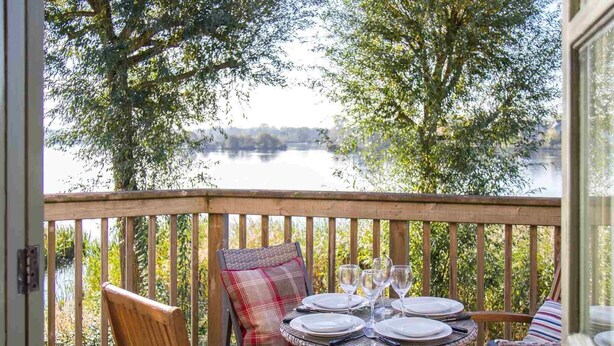 Une terrasse en bois avec une table dressée pour le repas, donnant sur un lac.