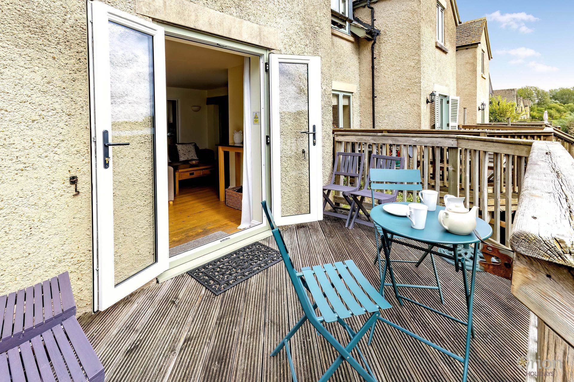 An open sliding door leading to a room with a wooden floor, a table with chairs, and a view of a building in the background.