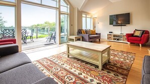 A spacious living room with a large window, a television, and a red sofa. - Spring Lake 77, The Ferns (P) - Lakeside Luxury, Hot Tub, Watersports, Sleeps 8 (South Cerney)