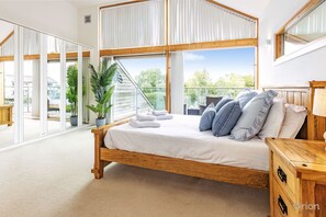 A bedroom with a wooden bed, white bedding, and a view of a lake through large windows.