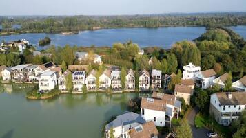 Un quartier résidentiel situé au bord d’un lac, avec des maisons dotées de balcons et de panneaux solaires, entouré d’une végétation luxuriante et bordé d’un lac paisible.