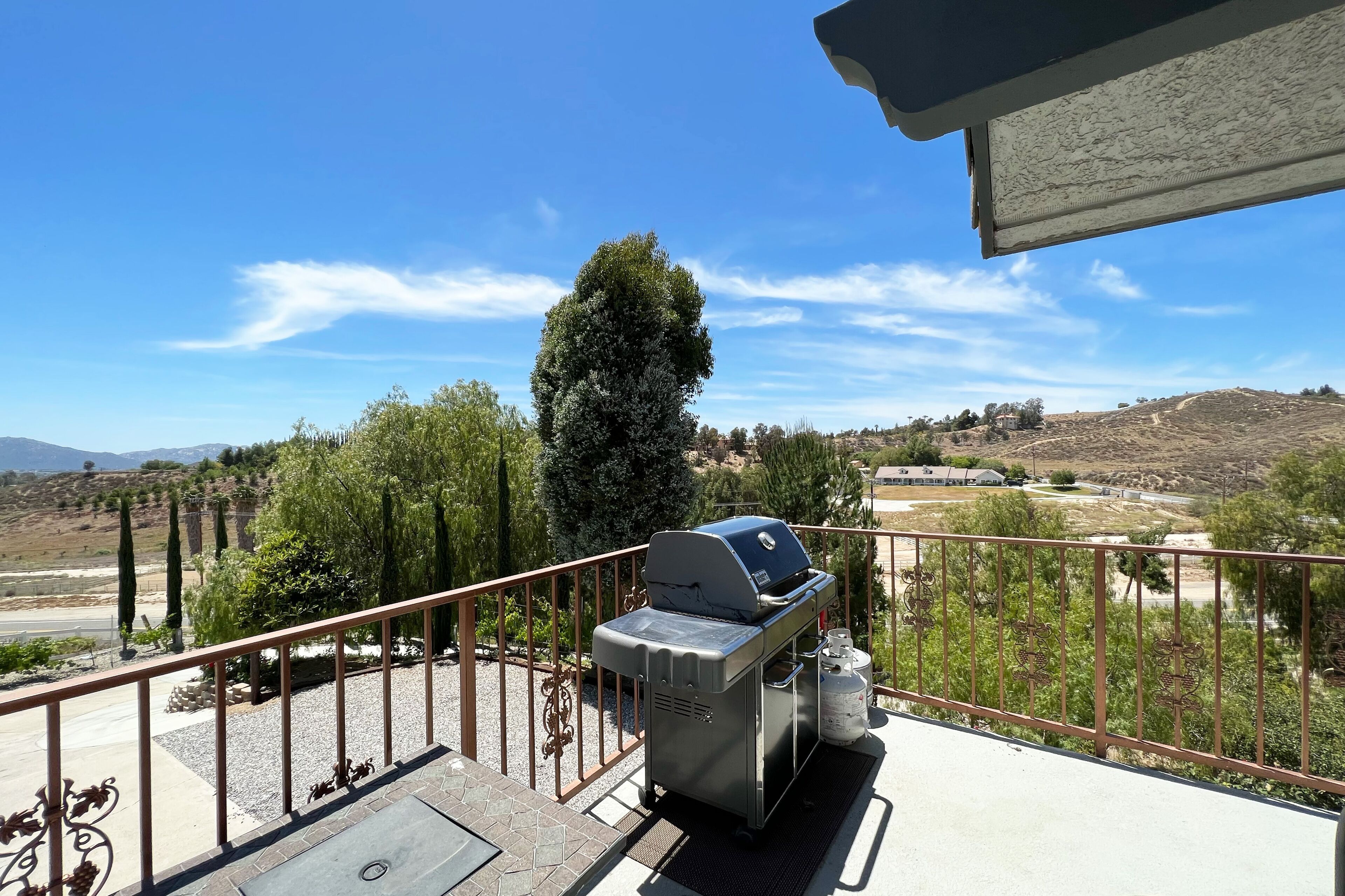 Ein Balkon mit Grill, Blick auf eine hügelige Landschaft und einem klaren, blauen Himmel.