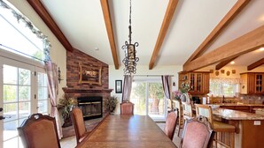 A spacious dining area with a long wooden table and chairs, a fireplace, and a kitchen with wooden cabinets and a large island. - House with pool/spa/minutes to wineries (Temecula)