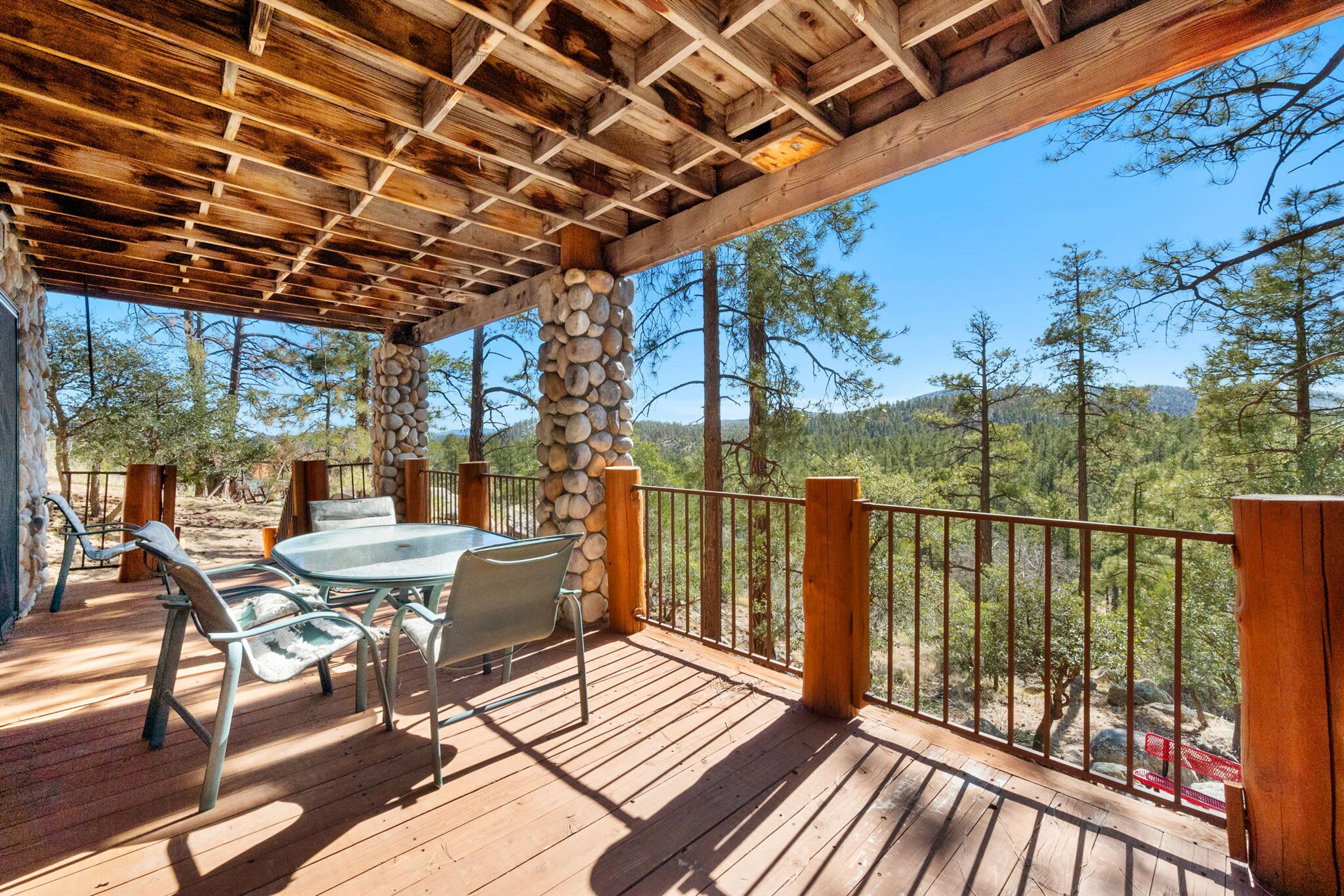 A wooden deck with a stone pillar, metal chairs, and a glass table.