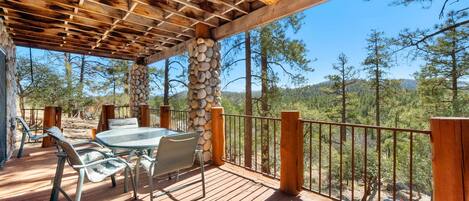 A wooden deck with a stone pillar, metal chairs, and a glass table.