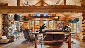 L’intérieur d’une cabane en rondins, avec une cheminée en pierre, des meubles en bois et de grandes fenêtres.