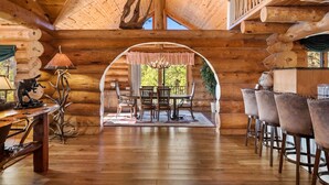 L’intérieur d’une cabane en rondins, avec un coin repas, un plafond en bois et une vue sur l’extérieur à travers une arche.