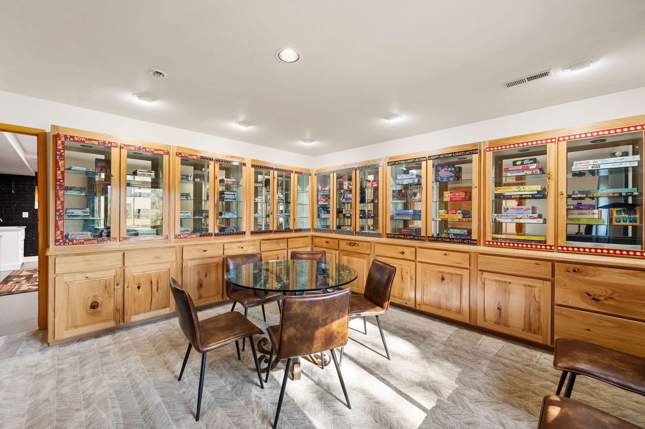 A spacious room with a round glass table surrounded by leather chairs, wooden cabinets with glass doors displaying various items, and a tiled floor.