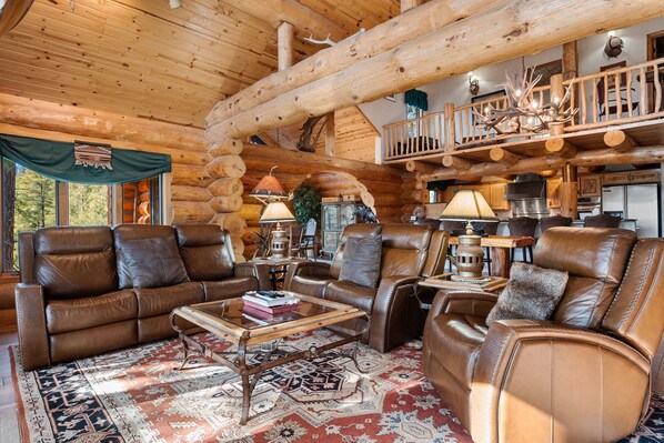 L’intérieur d’une cabane en rondins, avec des canapés en cuir, une table basse et un lustre.