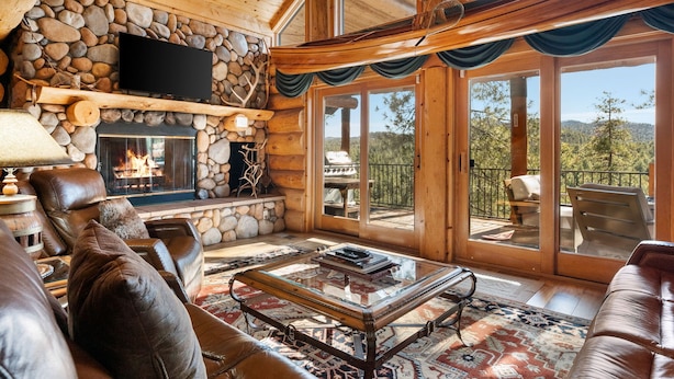 L’intérieur chaleureux d’un chalet en bois, avec une cheminée en pierre, des meubles en cuir et une grande fenêtre offrant une vue panoramique.