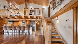 Un intérieur spacieux en bois, avec un escalier central, un coin repas avec des chaises et une cuisine visible au fond.