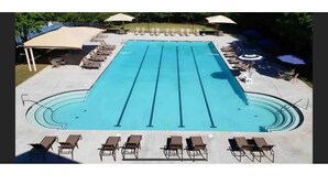 A swimming pool with multiple lanes, sun loungers, umbrellas, and a covered seating area.
