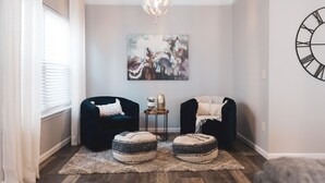 A cozy living room with two dark armchairs, a round coffee table, and a decorative painting on the wall.
