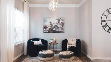 A cozy living room with two dark armchairs, a round coffee table, and a decorative painting on the wall.
