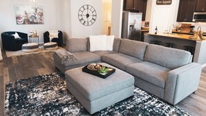 A modern living room with a sectional sofa, ottoman, and a decorative clock.