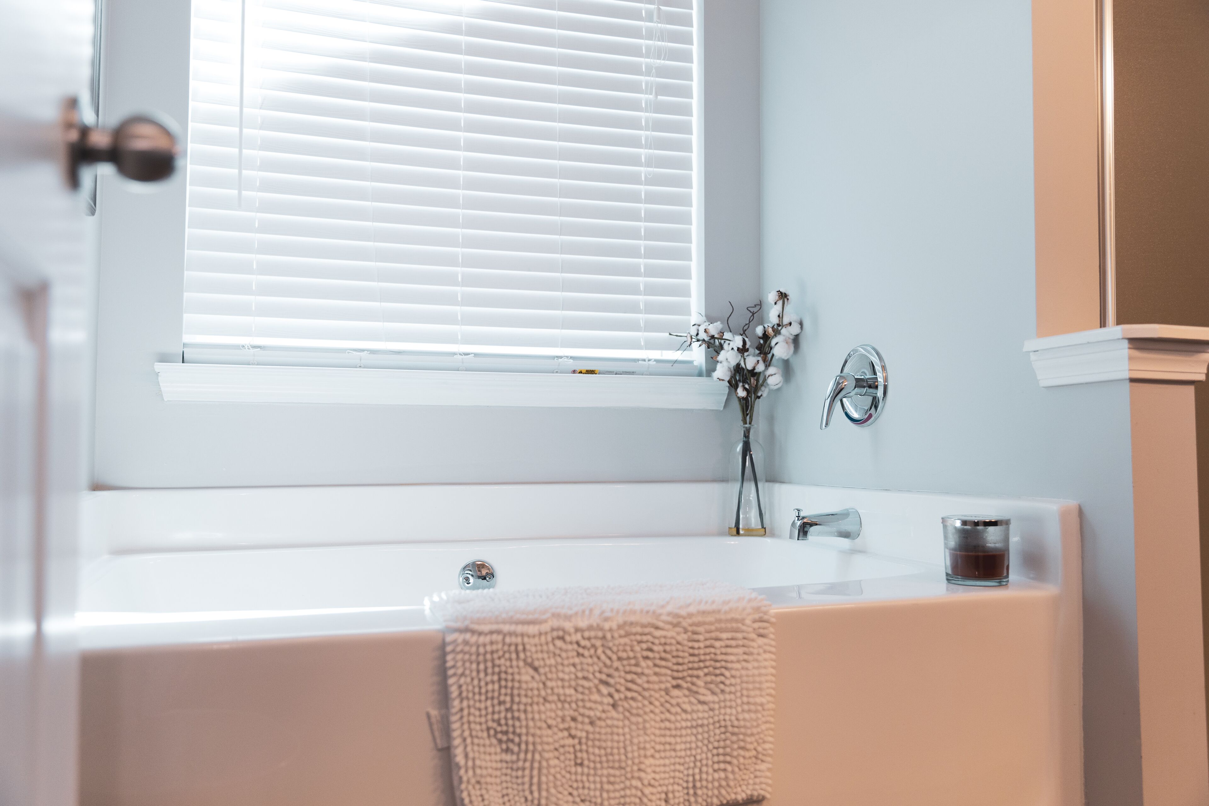 Ein Badezimmer mit einer Badewanne, einem Fenster mit Jalousien, einem Handtuch und einer Glaslaterne am Waschbecken.