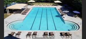 A swimming pool with multiple lanes, sun loungers, umbrellas, and a covered seating area.