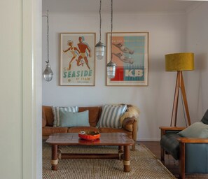 Un salon avec un canapé marron, des coussins à rayures, une table basse en bois et deux affiches accrochées au mur.