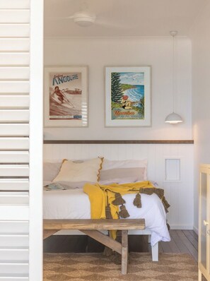 A bedroom with a bed, a bedside table, a lamp, and two framed posters on the wall.