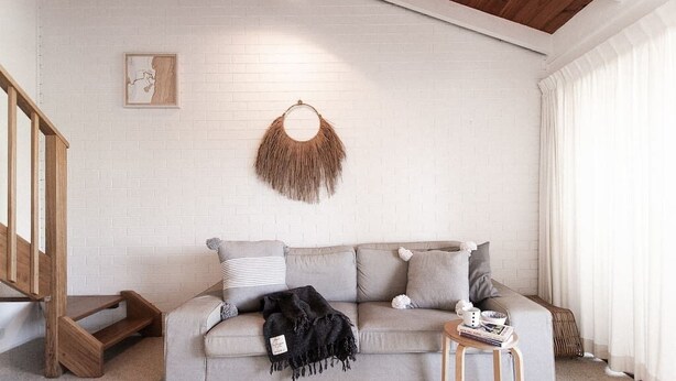 A living room with a grey sofa, a small wooden table, and a white brick wall. - BAY PROPERTIES | The Loft Yamba (Yamba)