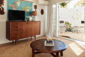 Een woonkamer met een houten kast, een ronde salontafel, een wereldkaart en uitzicht op een terras met stoelen en planten.