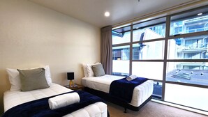 A hotel room with two beds, a large window with a city view, and a nightstand with a lamp. - U Suites on Jessie (Wellington)