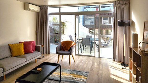 A modern living room with a sofa, armchair, and a coffee table. There is a sliding glass door leading to an outdoor balcony. - U Suites on Jessie (Wellington)