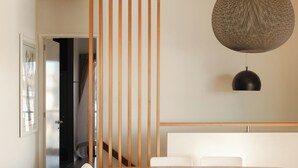 A modern living room with a sofa, a dining table with chairs, a hanging light fixture, and a wooden partition. - BAY PROPERTIES | The Chill (Yamba)